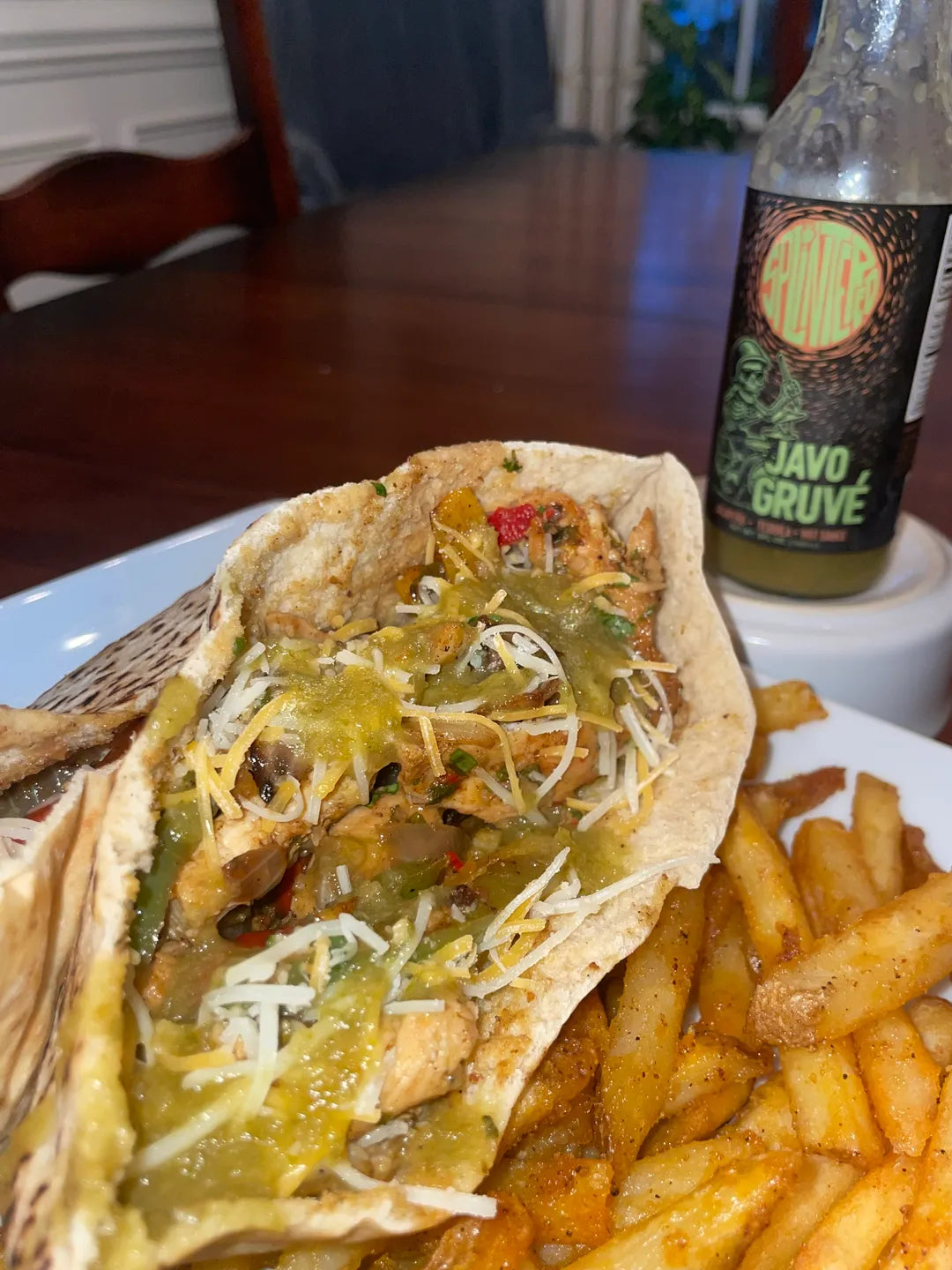 Tortilla with filling and cheese on a plate with French fries and a bottle of Javo Gruvé in the background.