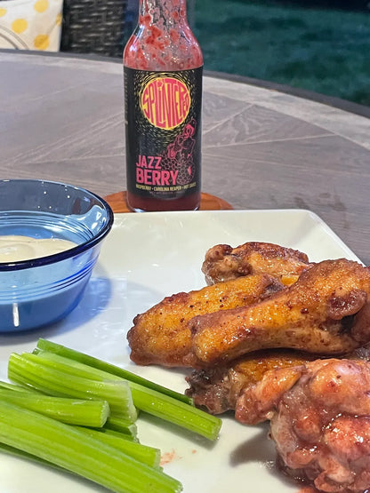 Wings with celery and a bottle of Splintered Jazz Berry hot sauce on a table