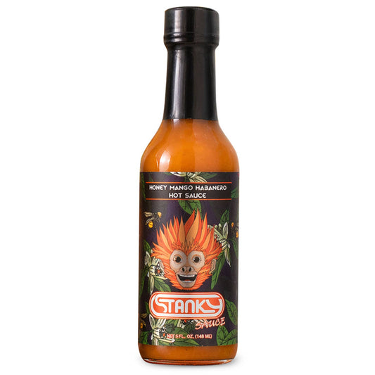 A bottle of Stanks Sauce Honey Mango-Hisbango Hot Sauce on a solid white background. The bottle contains a vibrant orange-red sauce and features a black cap and a black label with a cartoon monkey face and green leafy accents.