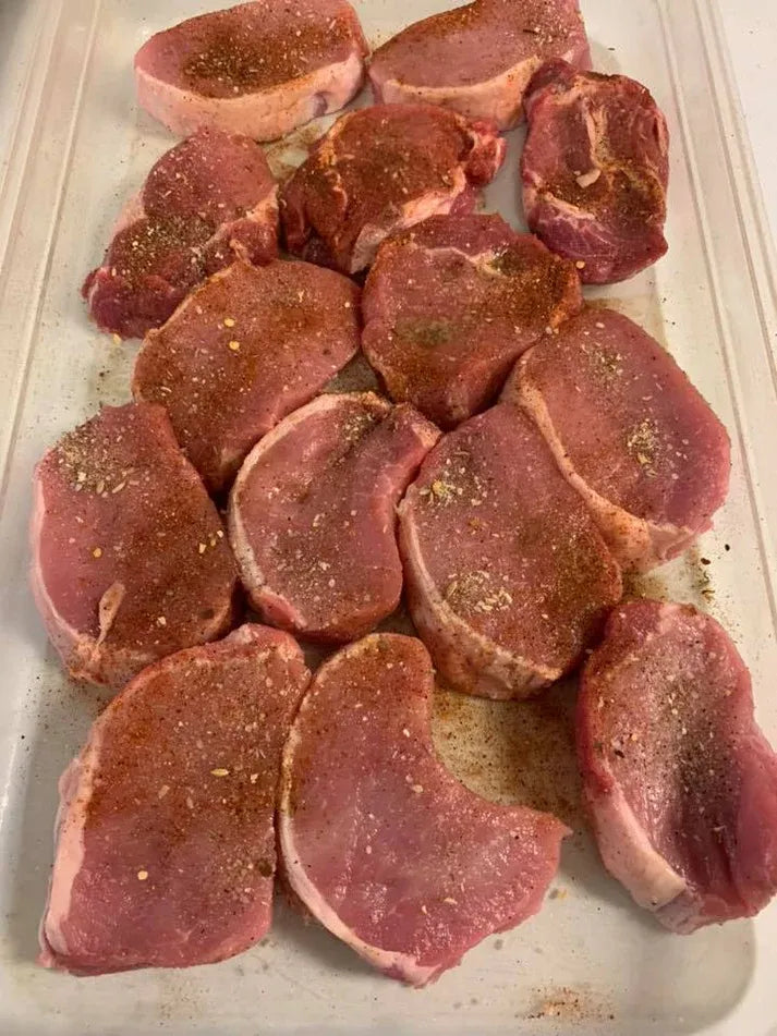 Raw pork chops seasoned with spices on a white cutting board