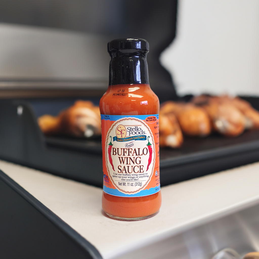 Bottle of Stella Foods Buffalo Wing Sauce on a grill with wings in the background