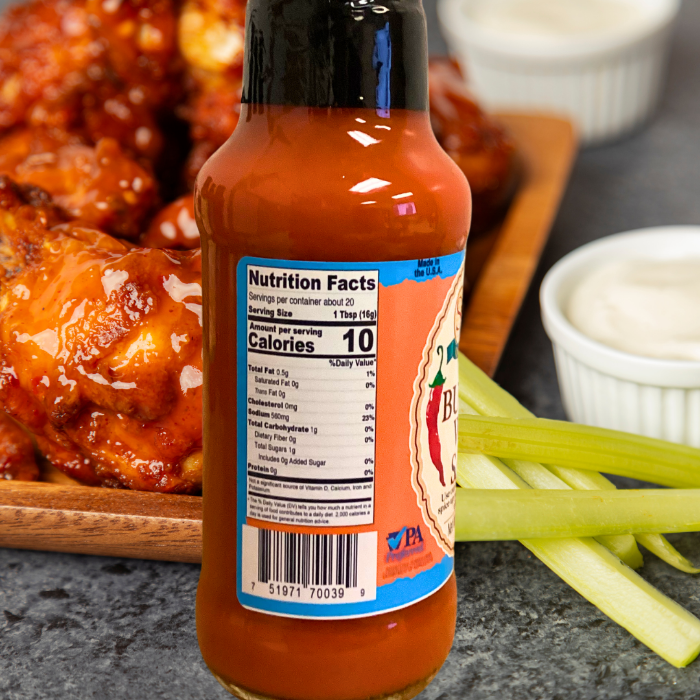 Bottle of Stello Foods hot sauce with nutrition label on a table with wings and celery sticks.