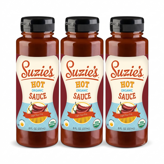 Three bottles of Suzie's Hot Organic Sauce arranged side by side on a plain white background. Each bottle has a black cap and a label with red, cream, and light blue sections showing the product name and branding.