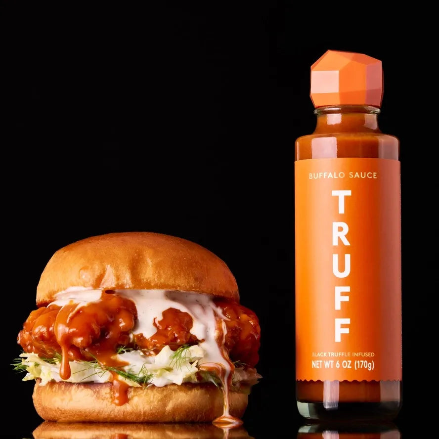 Burger with buffalo sauce and a bottle of TRUFF buffalo sauce on a black background