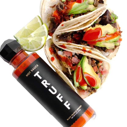Tacos with various fillings on a plate with a bottle of Truff hot sauce.