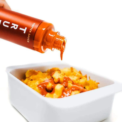 Orange bottle of hot sauce being poured onto macaroni and cheese