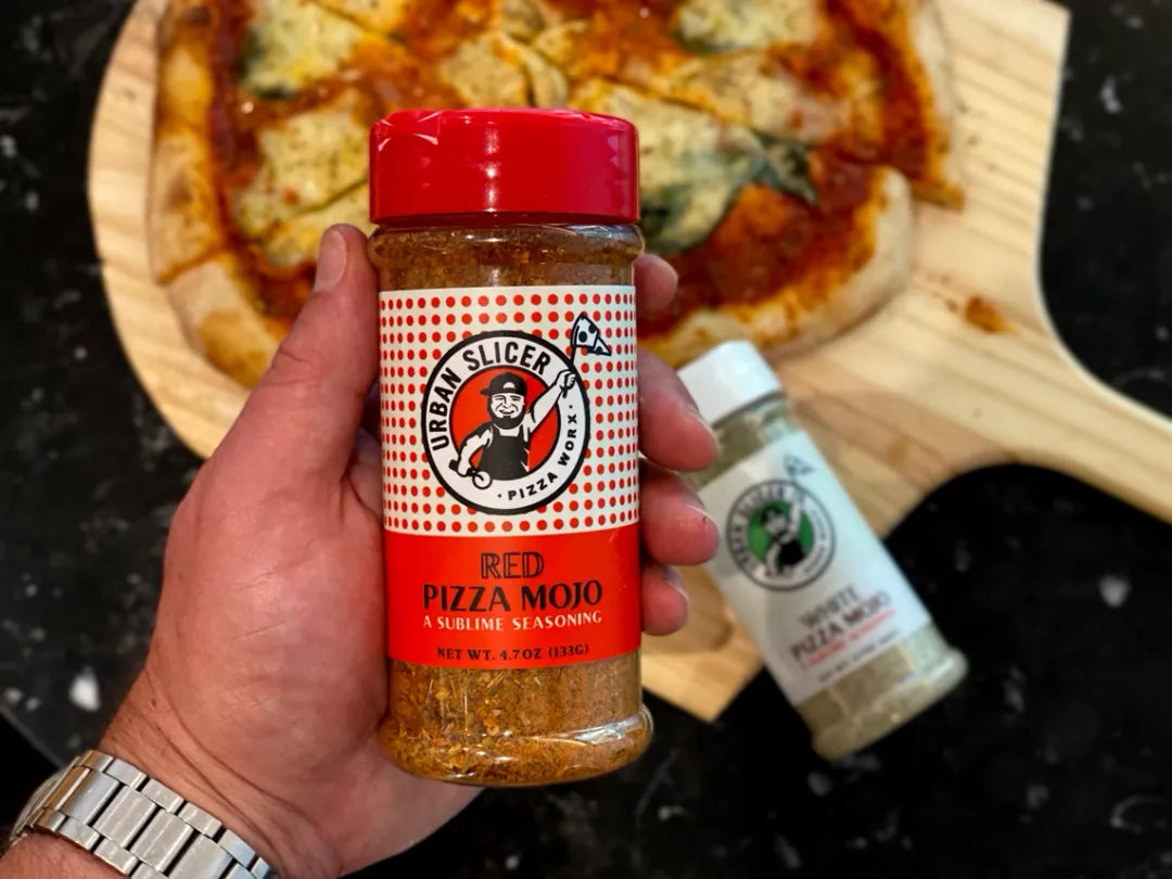 Hand holding a jar of Urban Slicer Red Pizza Mojo with a pizza in the background