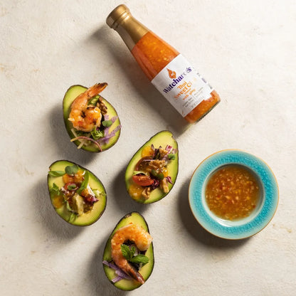 Avocado boats with shrimp and a bottle of hot sauce on a light background