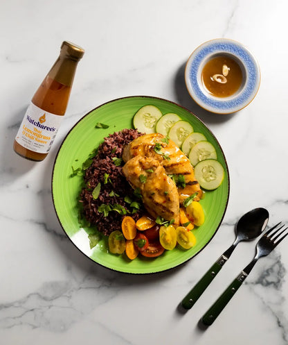 Green plate with chicken, rice, and vegetables on a marble surface with a bottle of sauce.