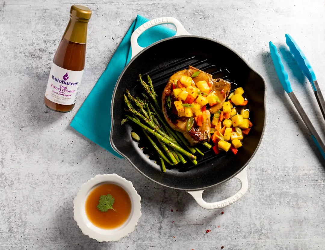 Dish with steak, asparagus, and peach salsa on a gray surface with a bottle of watcharee teriyaki sauce.