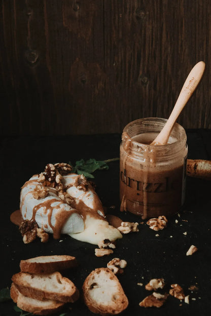 Jar of Cinnamon Honey with a wooden spoon, bread slices, and walnuts on a dark surface.