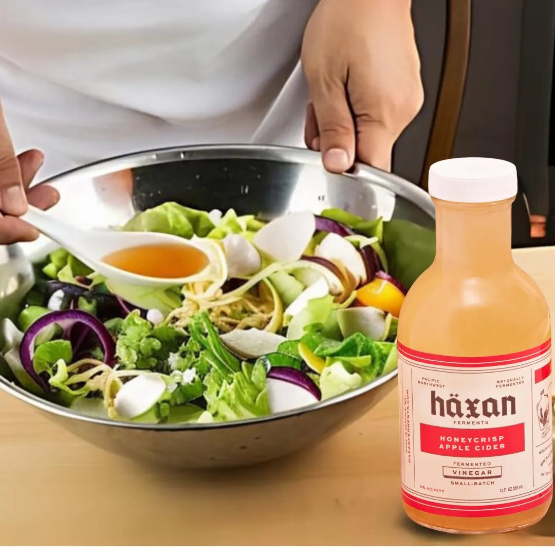 Person preparing a salad with a bottle of Häxan Honeycrisp Apple Cider Vinegar.