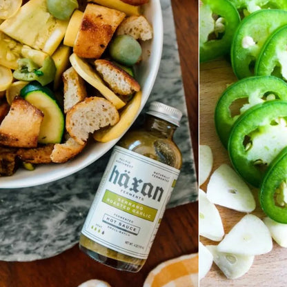 Bowl of salad with croutons and a bottle of Häxan hot sauce, surrounded by sliced jalapeños and onions.