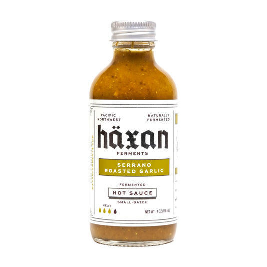 Bottle of Häxan Serrano Roasted Garlic Hot Sauce on a white background
