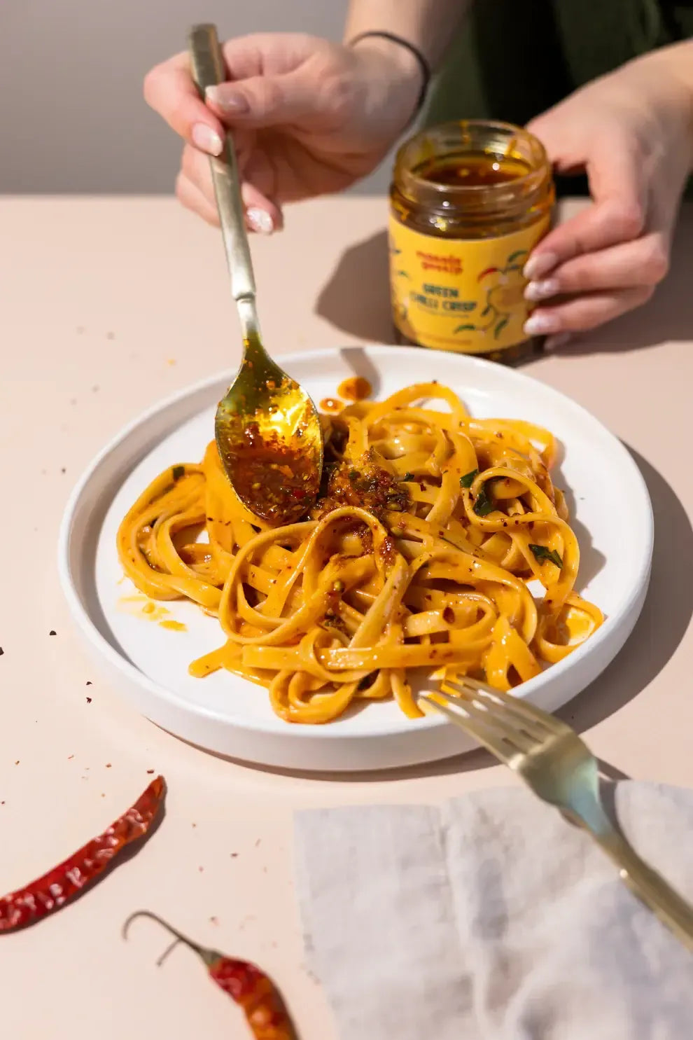 Plate of pasta with a fork and spoon, person holding a jar of sauce.