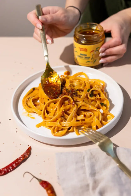 Plate of pasta with a fork and spoon, person holding a jar of sauce.