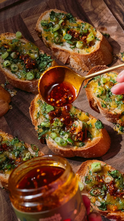 Bruschetta with a spoon drizzling sauce over it on a wooden board