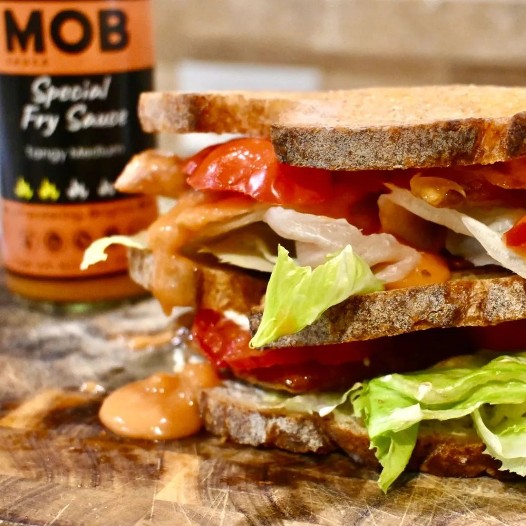 Sandwich with various ingredients on a wooden board next to a bottle of Special Fry Sauce.
