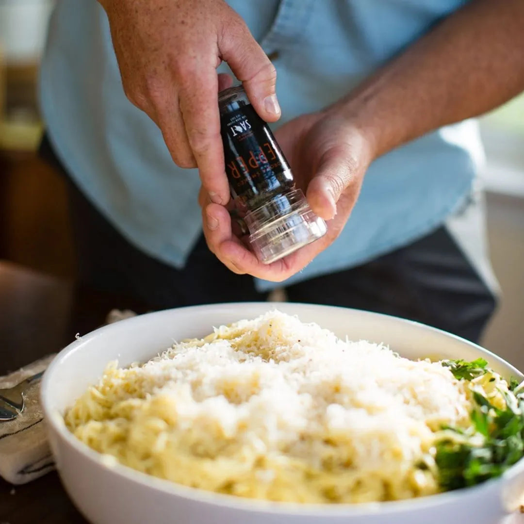 Person seasoning a bowl of pasta with a pepper grinder.