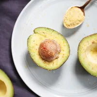 Two halves of a avocado on a white plate with a spoonful of a beige substance.