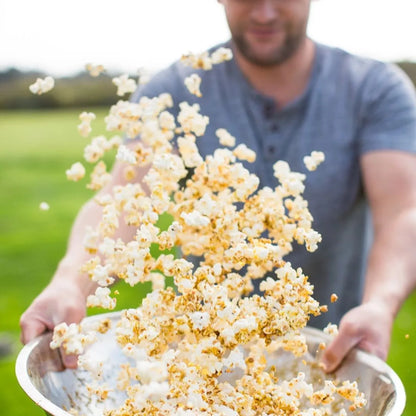 Man holding a tray of popcorn with a blurred outdoor background